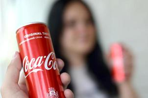 Jarkov. ucrania - 2 de mayo de 2019 mujer feliz levanta lata de coca-cola con un amigo en el interior del garaje foto