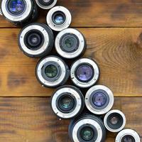 Several photographic lenses lie on a brown wooden background. Space for text photo