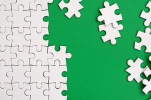 Fragment of a folded white jigsaw puzzle and a pile of uncombed puzzle elements against the background of a green surface. Texture photo with space for text