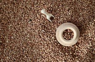 Background image of a large pile of buckwheat, in the middle of which lies a small jug and a wooden spatula for cereals photo