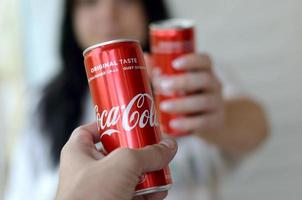 KHARKOV. UKRAINE - MAY 2, 2019 Happy woman raise Coca-Cola tin can with male friend in garage interior photo