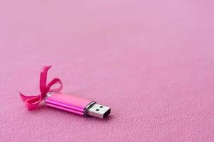 la tarjeta de memoria flash usb de color rosa brillante con un lazo rosa yace sobre una manta de suave y peluda tela de vellón rosa claro. diseño clásico de regalo femenino para una tarjeta de memoria foto