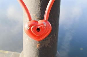 A red barn lock in the shape of a heart hangs on the railing of a bridge. Wedding tradition to hang locks on bridges for eternal love photo