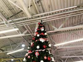 Festive green beautiful elegant Christmas tree with balls for the New Year on the background of the ceiling with metal ventilation pipes in the loft style. Concept Christmas at an industrial plant photo