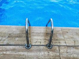 escalera de metal cromado con barandilla para descender a la piscina para nadar y bañarse con agua tibia azul clara y limpia en un hotel en un paraíso tropical foto