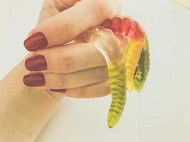 long, mouth-watering, multi-colored worms on the hand of a girl with a bright red manicure. the worms lie on the fingers. bulky, structural worms, ribbed shape photo