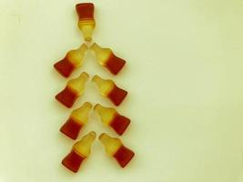 Christmas tree made from gummy bottles with lemonade on a white matte background. at the top of the tree is a large top of candy. symbolic christmas tree photo