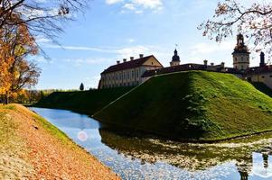 Old, ancient medieval castle with spiers and towers, walls of stone and brick surrounded by a protective moat with water in the center of Europe. Baroque style architecture photo