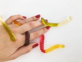long, mouth-watering, multi-colored worms lie on the girl's hand with a bright red manicure. green, yellow, brown and transparent candy worms crawl along the hand photo