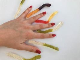 gusanos largos, deliciosos y multicolores en la mano de una chica con una manicura roja brillante. los gusanos yacen entre los dedos. servicio de postre inusual. dulces deliciosos foto