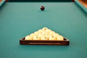 Green billiard sports table with billiards, a pool with a white and black ball and a triangle photo