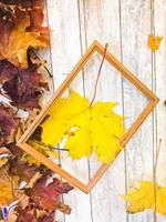 Wooden rectangular picture frame and yellow colorful natural autumn leaves, maple on the background of wooden boards. The background. Texture photo