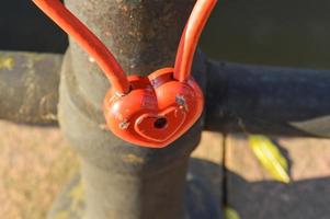 A red barn lock in the shape of a heart hangs on the railing of a bridge. Wedding tradition to hang locks on bridges for eternal love photo