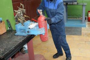 un trabajador masculino en un gran vicio industrial de metal está reparando un cilindro de extintor rojo en un taller en la planta foto