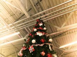 Festive green beautiful elegant Christmas tree with balls for the New Year on the background of the ceiling with metal ventilation pipes in the loft style. Concept Christmas at an industrial plant photo