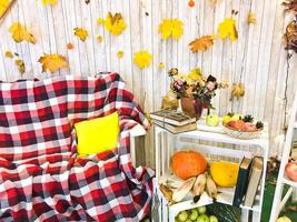 Checkered plaid on an armchair and a wooden table with vintage books tied with twine and a vase, herbarium, green apple on the background of wooden boards and yellow autumn leaves. photo