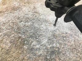 A sturdy, hard metal iron drill bit drills a hole in a large gray stone. Close view. The background photo