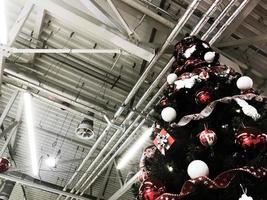 Festive green beautiful elegant Christmas tree with balls for the New Year on the background of the ceiling with metal ventilation pipes in the loft style. Concept Christmas at an industrial plant photo