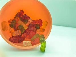 gummy bears of different colors lie in plastic and pink round shape. teddy bears are stacked in the kitchen in a kitchen sprinkler. candy on a matte colorful background photo