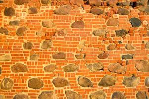 The texture of the old ancient medieval antique stone hard peeling cracked brick wall of rectangular red clay bricks and large stones, cobblestones. The background photo