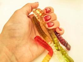 a lot of gummy worms lie on the girl's hand. bright, red, glossy manicure on an orange matte background. gelatinous worms lie in the palm of your hand photo