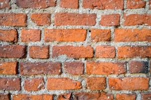 The texture of the old ancient medieval antique sturdy stone peeling scratched wall of rectangular red orange bright brick with seams and cracks. The background photo