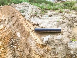 earth, dirt with marks from the wheels of cars. mud furrows. construction site, lots of sand and embankment. next to it lies a black round metal pipe photo