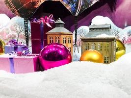 round, glass, multi-colored balls lie on the white snow. showcase decoration. small miniature houses and artificial snow. cute decorations to create a Christmas mood photo