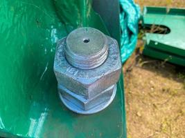 Two nuts are screwed onto a large iron metal stainless mounted threaded bolt. Close view photo