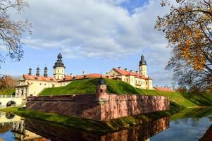 Old, ancient medieval castle with spiers and towers, walls of stone and brick surrounded by a protective moat with water in the center of Europe. Baroque style architecture photo