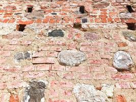 The texture of the old ancient medieval antique stone hard peeling cracked brick wall of rectangular red clay bricks and large stones, cobblestones. The background photo