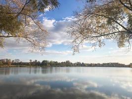 hermoso paisaje otoñal con árboles y hojas amarillas en el lago contra el cielo azul en un día soleado foto