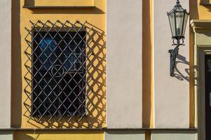 A large rectangular window of a yellow stone building closed by a large black iron grate. The background photo