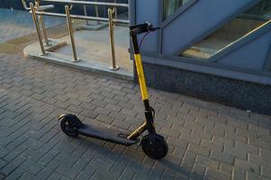 un scooter eléctrico amarillo brillante se encuentra en el centro de la ciudad para que la gente viaje. alquiler de transporte para el movimiento. cargado de la red eléctrica. Fabricado con materiales antivandálicos. el fondo del pavimento de asfalto foto