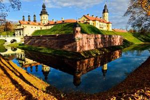 Old, ancient medieval castle with spiers and towers, walls of stone and brick surrounded by a protective moat with water in the center of Europe. Baroque style architecture photo