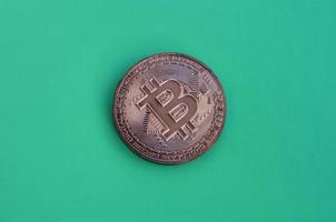 Chocolate product in the form of physical bitcoin lies on a green plastic background. Model of the crypto currency in the edible form photo