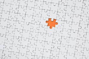 The texture of a white jigsaw puzzle in an assembled state with one missing element forming an orange space photo