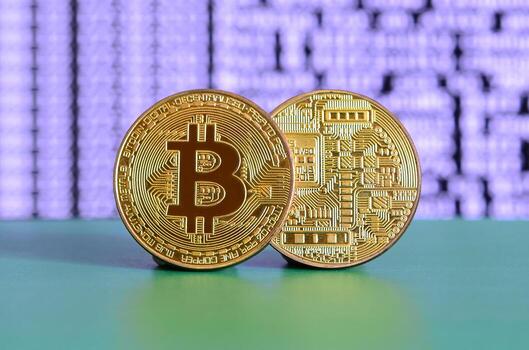 Two gold bitcoins lie on the green surface on the background of the display, which shows the process of mining the crypto currency photo