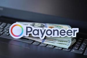 TERNOPIL, UKRAINE - SEPTEMBER 6, 2022 Payoneer paper logotype lies on black laptop with US dollar bills. Payoneer is American financial services company that provides online money transfer photo