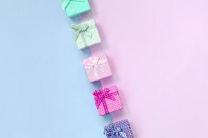 Small gift boxes of different colors with ribbons lies on a violet and pink background photo