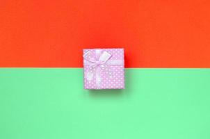 Small pink gift box lie on texture background of fashion pastel turquoise and red colors paper photo