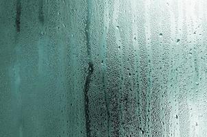 textura de una gota de lluvia sobre un fondo transparente húmedo de vidrio. tonificado en color turquesa foto