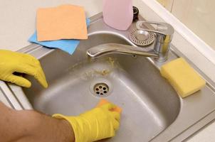 Person or householder cleaning the kitchen sink with sponge in close up view photo