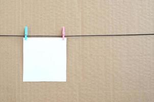 White blank card on rope on a brown cardboard background. Creative reminder, small sheet of paper on wooden clothespin, memo backdrop photo