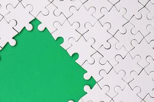 Fragment of a folded white jigsaw puzzle on the background of a green plastic surface. Texture photo with copy space for text