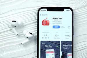 kharkov, ucrania - 5 de marzo de 2021 icono de radio fm y aplicación de la tienda de aplicaciones en la pantalla de visualización del iphone 12 pro con airpods pro en la mesa blanca foto