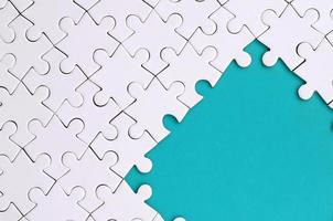 Fragment of a folded white jigsaw puzzle on the background of a blue plastic surface. Texture photo with copy space for text