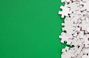 A pile of uncombed elements of a white jigsaw puzzle lies on the background of a green surface. Texture photo with copy space for text