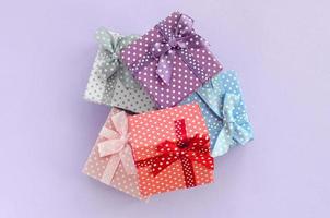 Pile of a small colored gift boxes with ribbons lies on a violet background. Minimalism flat lay top view photo