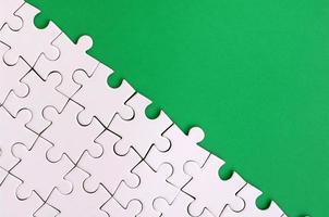 Fragment of a folded white jigsaw puzzle on the background of a green plastic surface. Texture photo with copy space for text